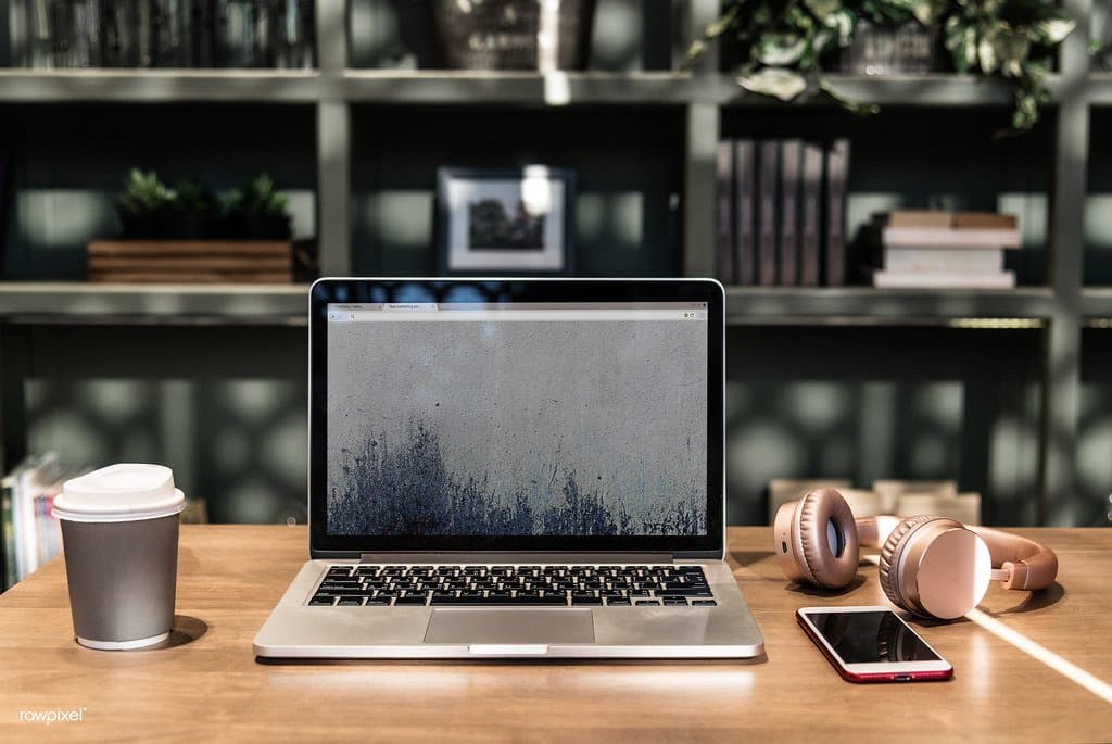 A laptop, coffee cup, and wireless headphones on a desk in a modern coworking space
